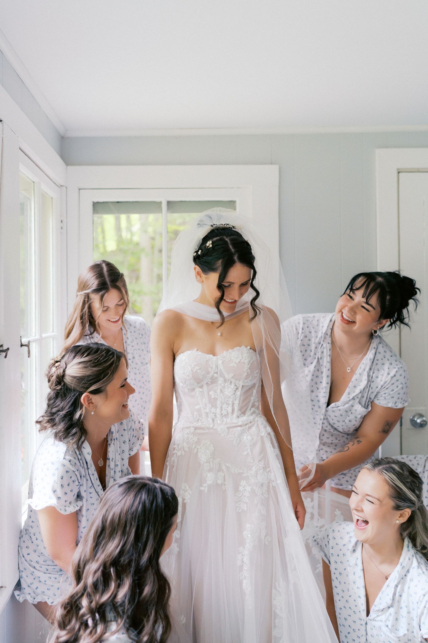 Bridesmaids in floral dresses share joyful laughter with bride in white gown during wedding preparations.
