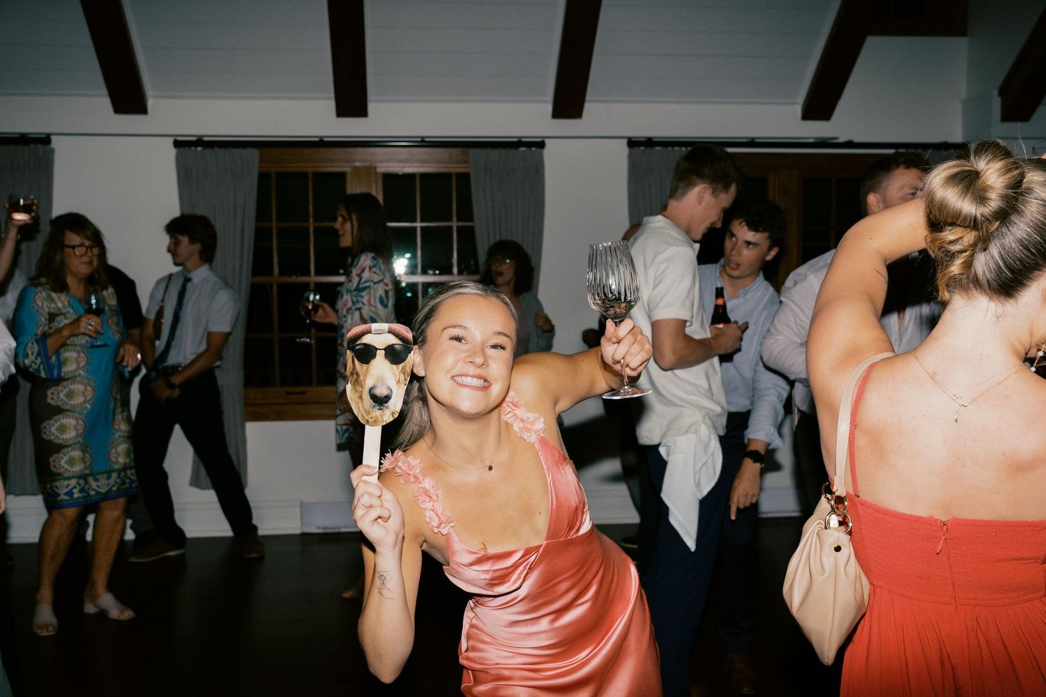 A group of wedding guests dancing and celebrating with drinks at a reception party.