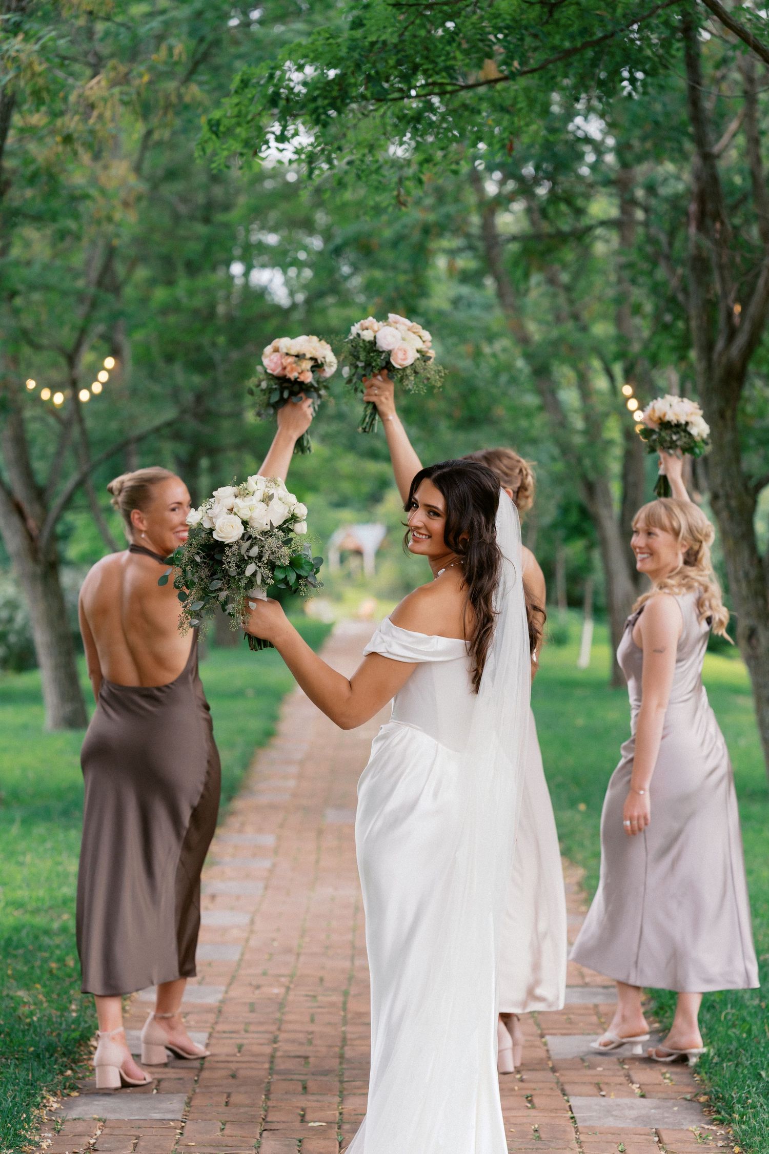 Wedding party celebrating on a brick path surrounded by trees and string lights.