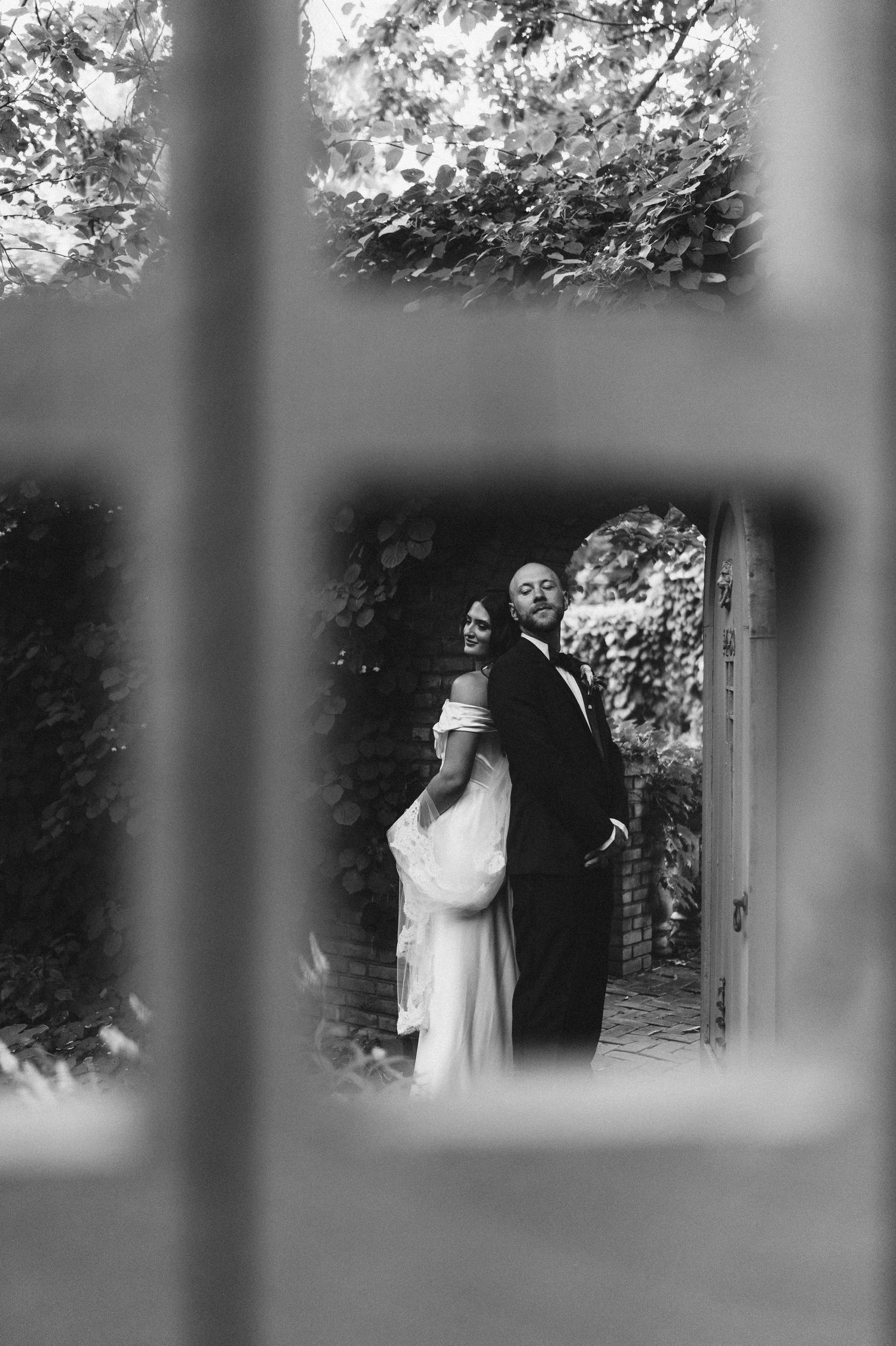 Black and white photo of couple framed through window panes in garden setting.