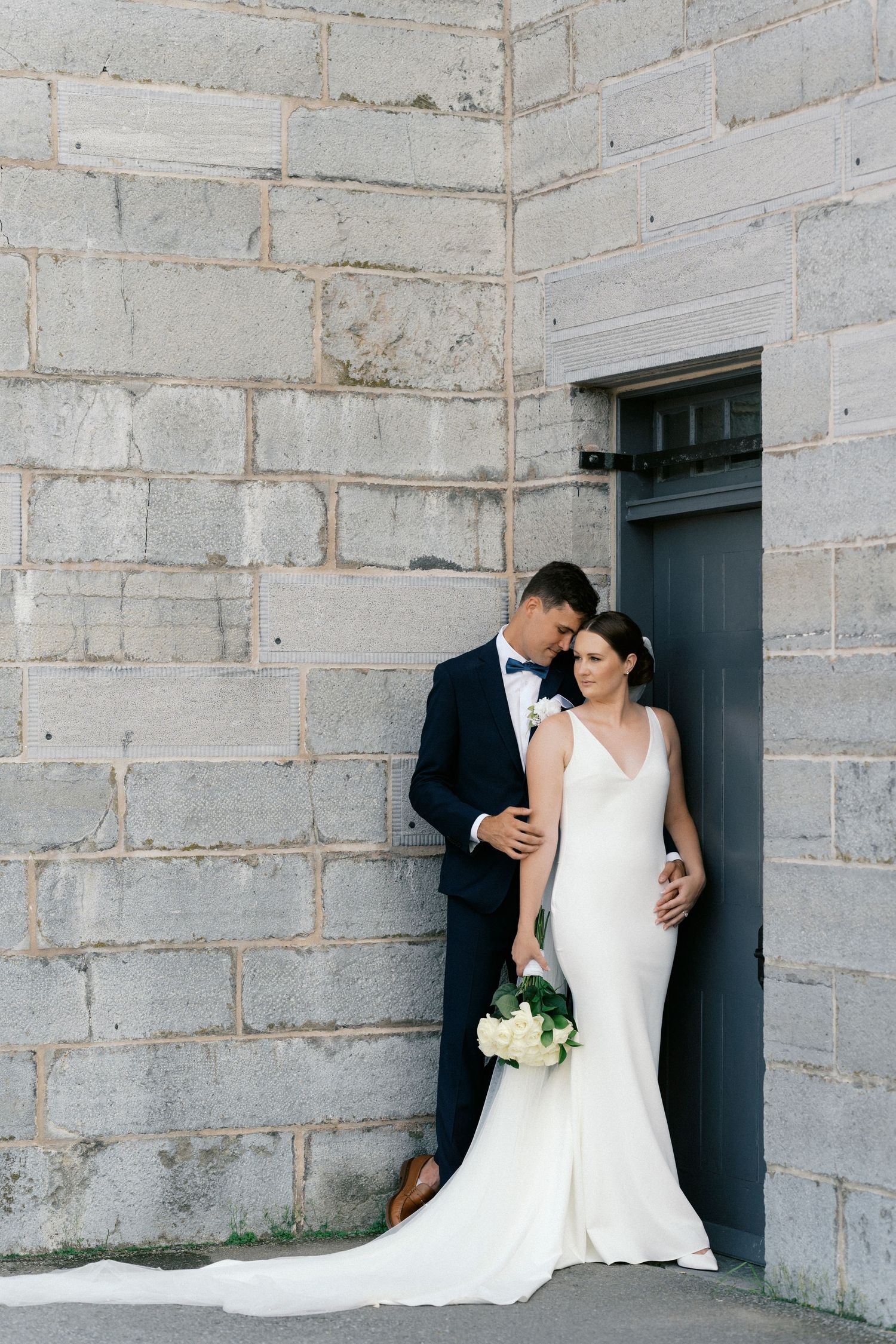 Elegant wedding portrait against stone wall with classic black door framing the composition.