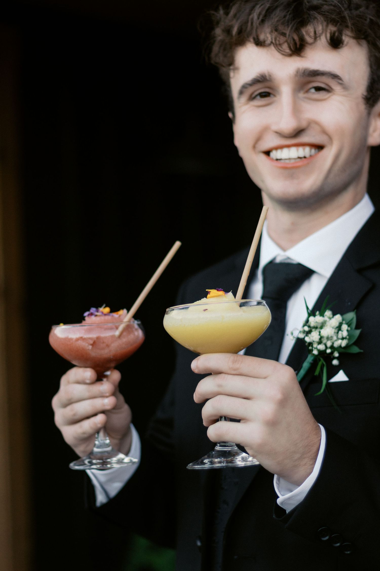 Colorful cocktails being held in formal attire with boutonniere detail.