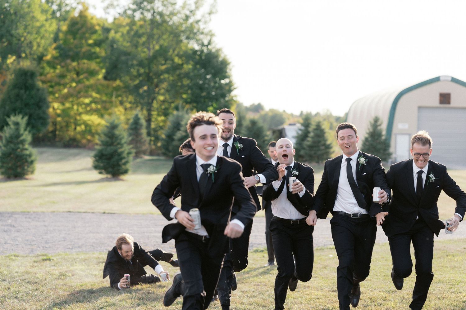 Groomsmen in black suits running playfully across a grassy field.