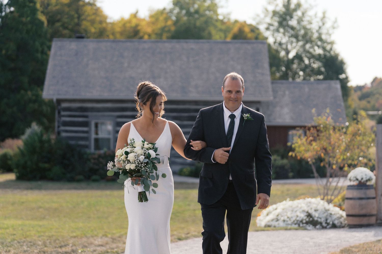 Wedding party walking along a path outside rustic buildings during an outdoor ceremony.