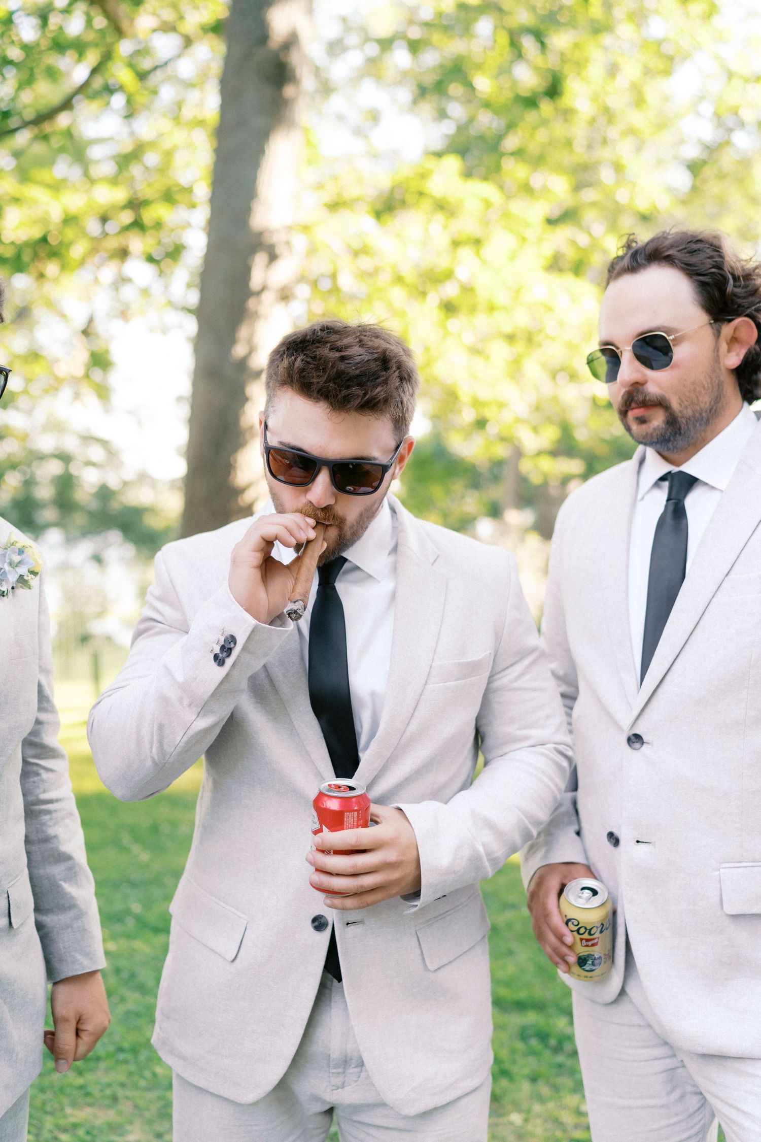 Groomsmen in light gray suits share drinks and laughs during outdoor wedding festivities.