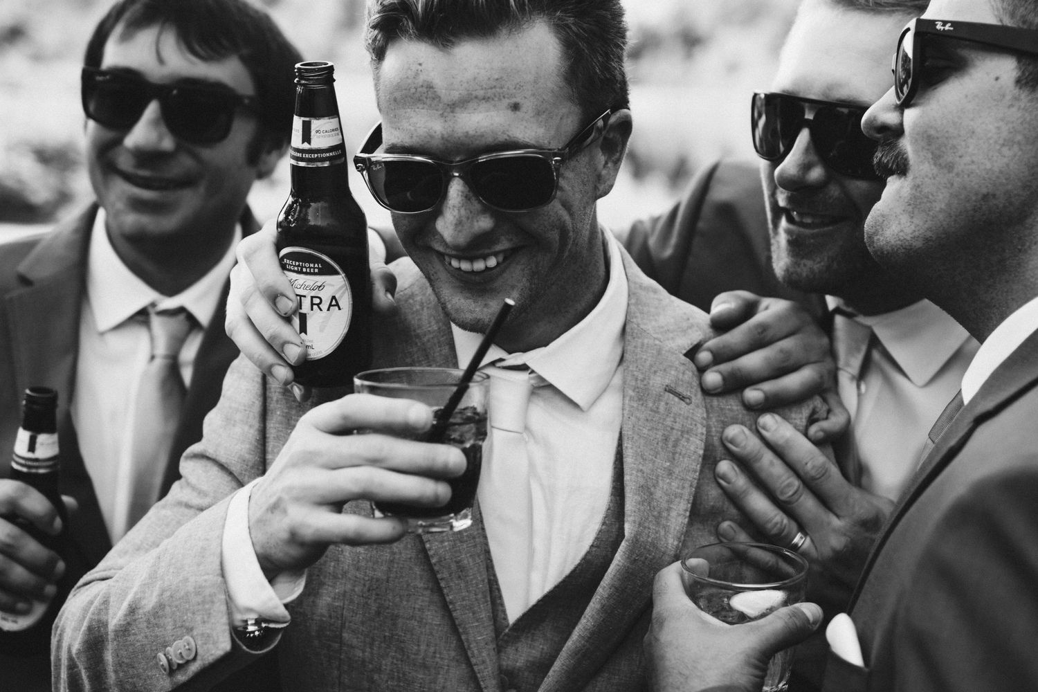 Groomsmen in sunglasses share drinks and laughs during wedding celebrations.
