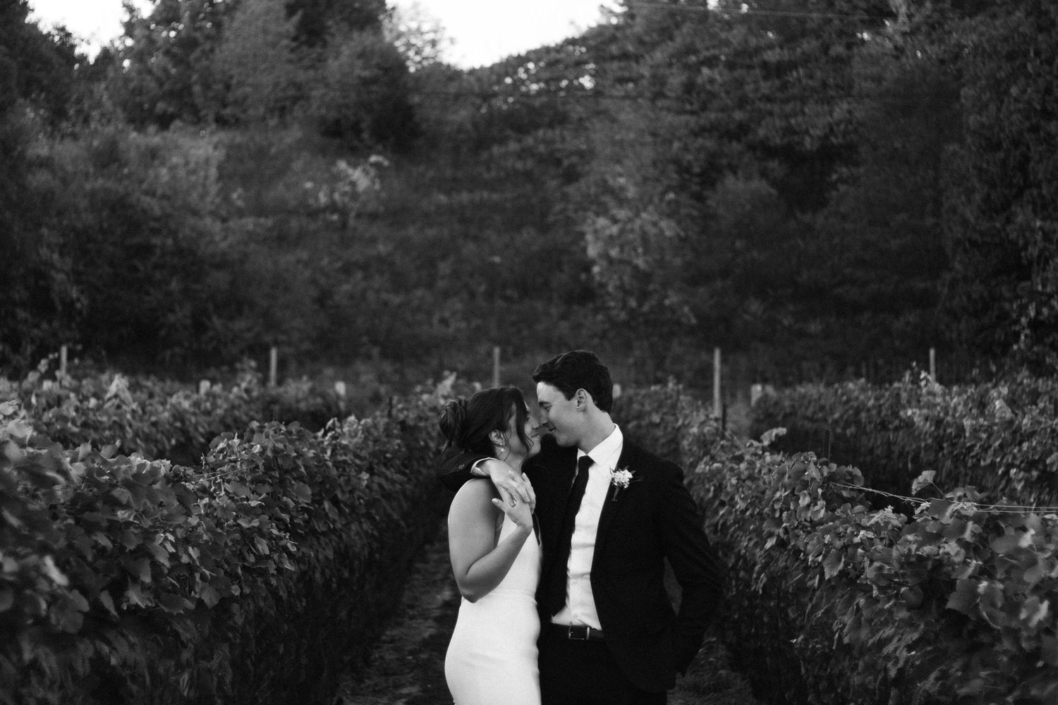 Black and white photo of a romantic moment between newlyweds in a garden setting.