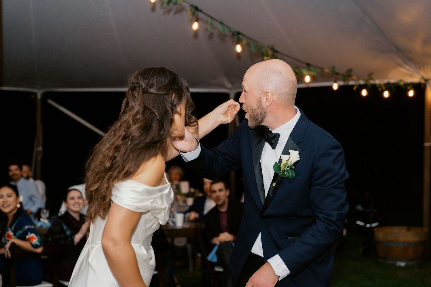 Couple shares a joyful moment dancing under string lights at their outdoor wedding reception.