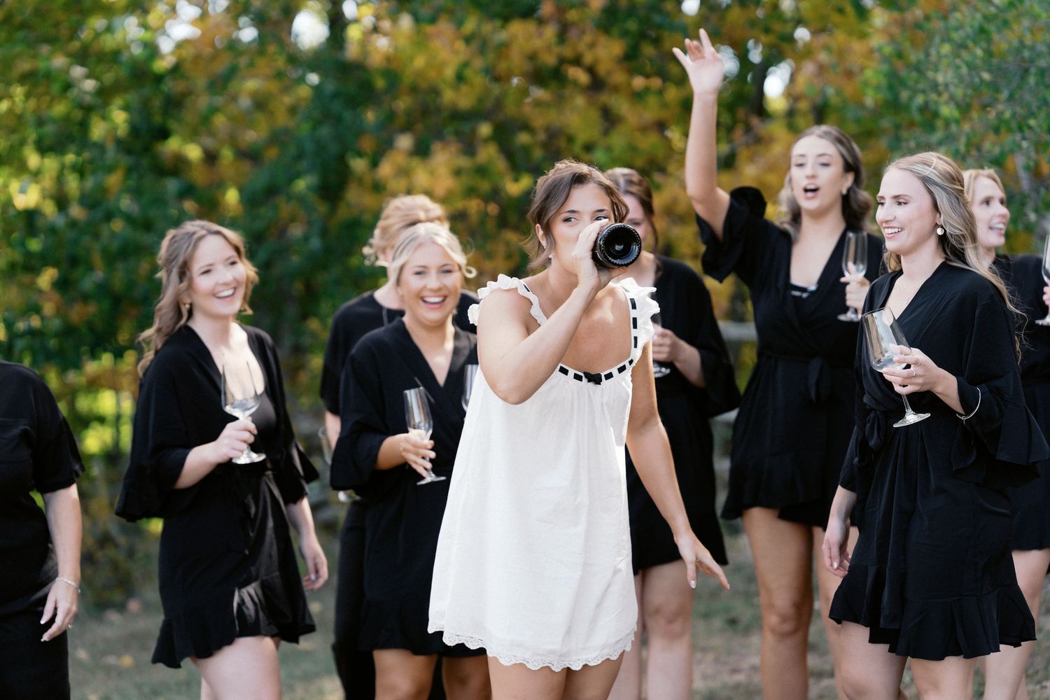 Bridesmaids in black dresses celebrating joyfully outdoors during a wedding photoshoot.