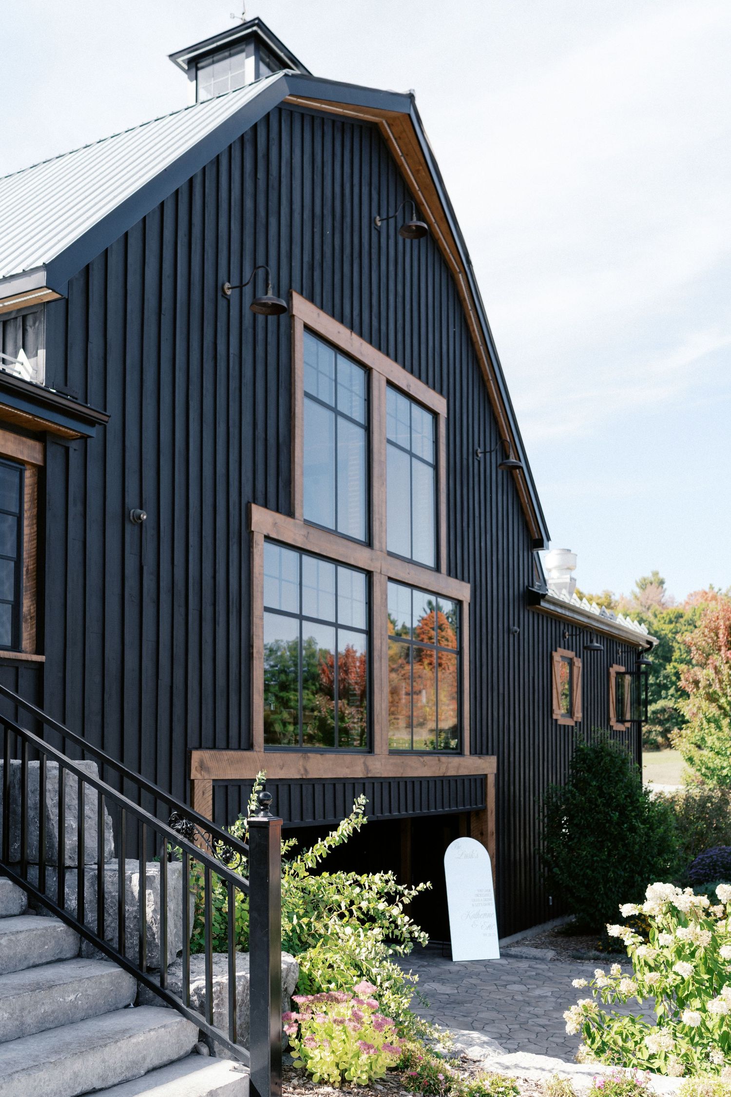 Modern black barn-style house with large windows and wooden accents surrounded by landscaping.