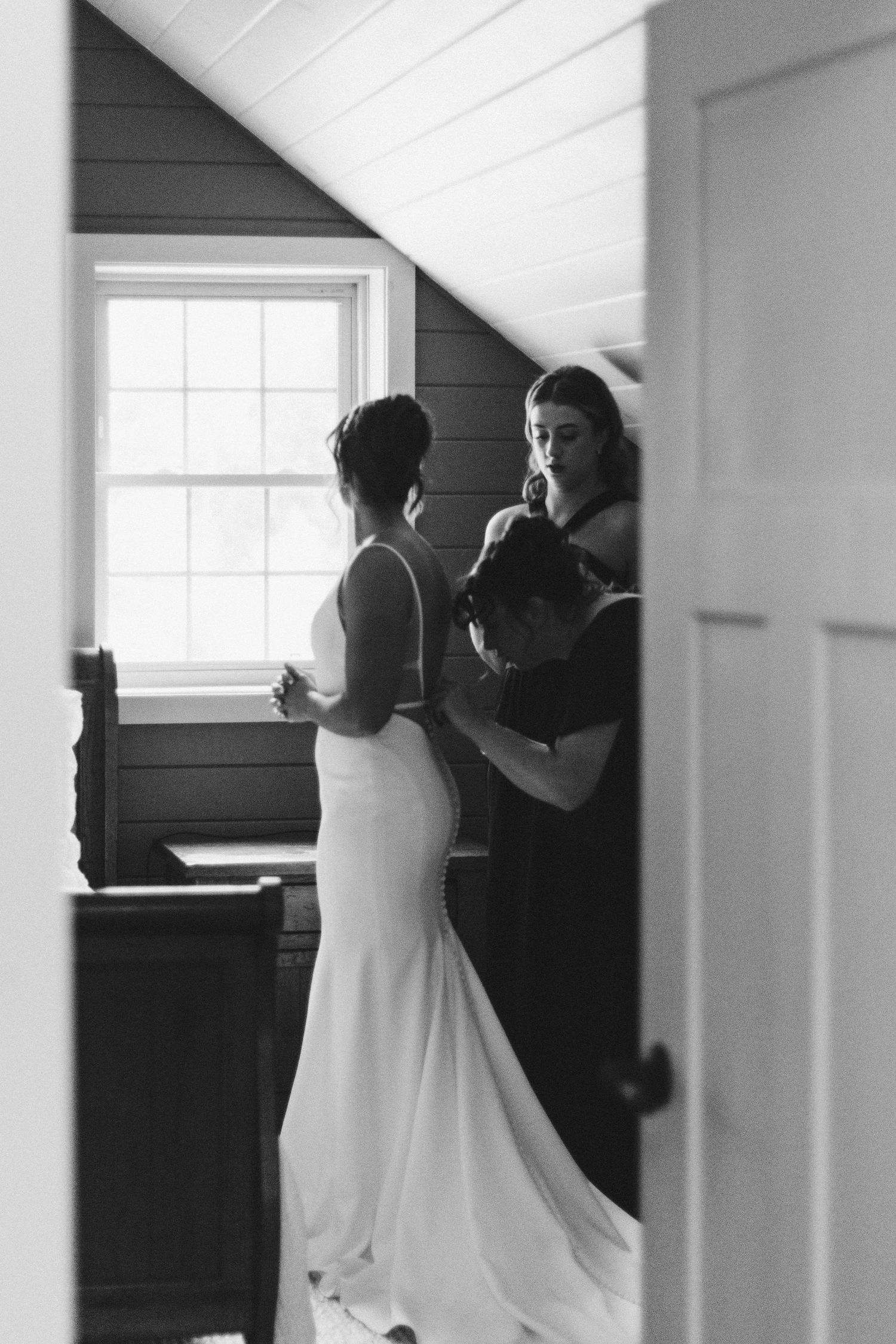 Black and white photo of two people in a sunlit room, one wearing a fitted white wedding dress.
