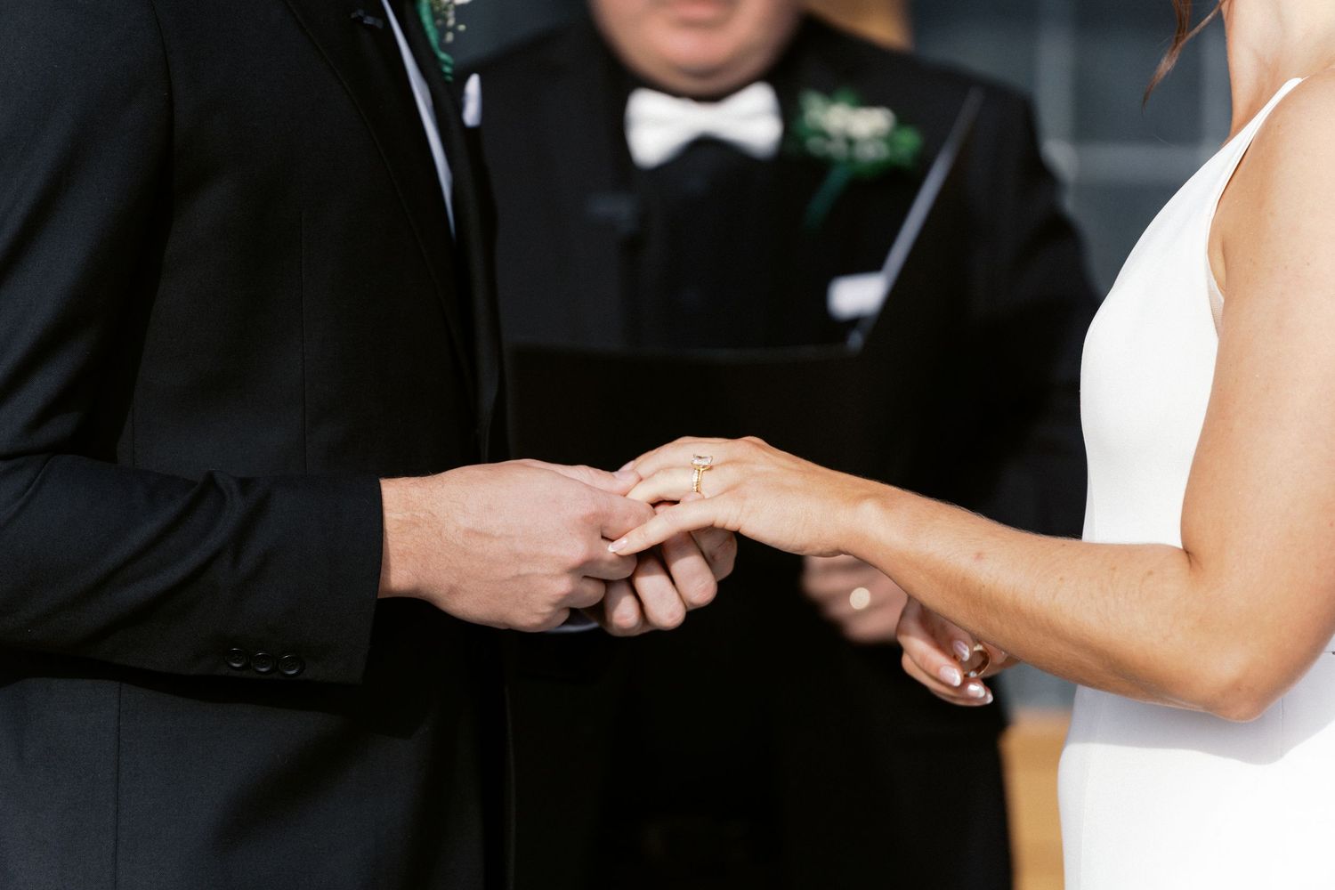 Close-up of hands exchanging wedding rings during ceremony.