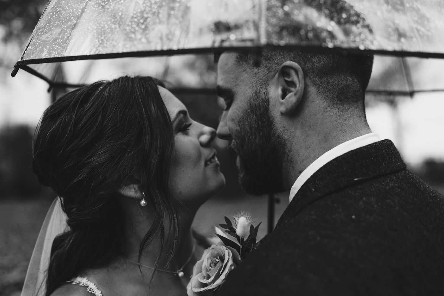 Romantic black and white portrait of newlyweds sharing an intimate moment under an umbrella.