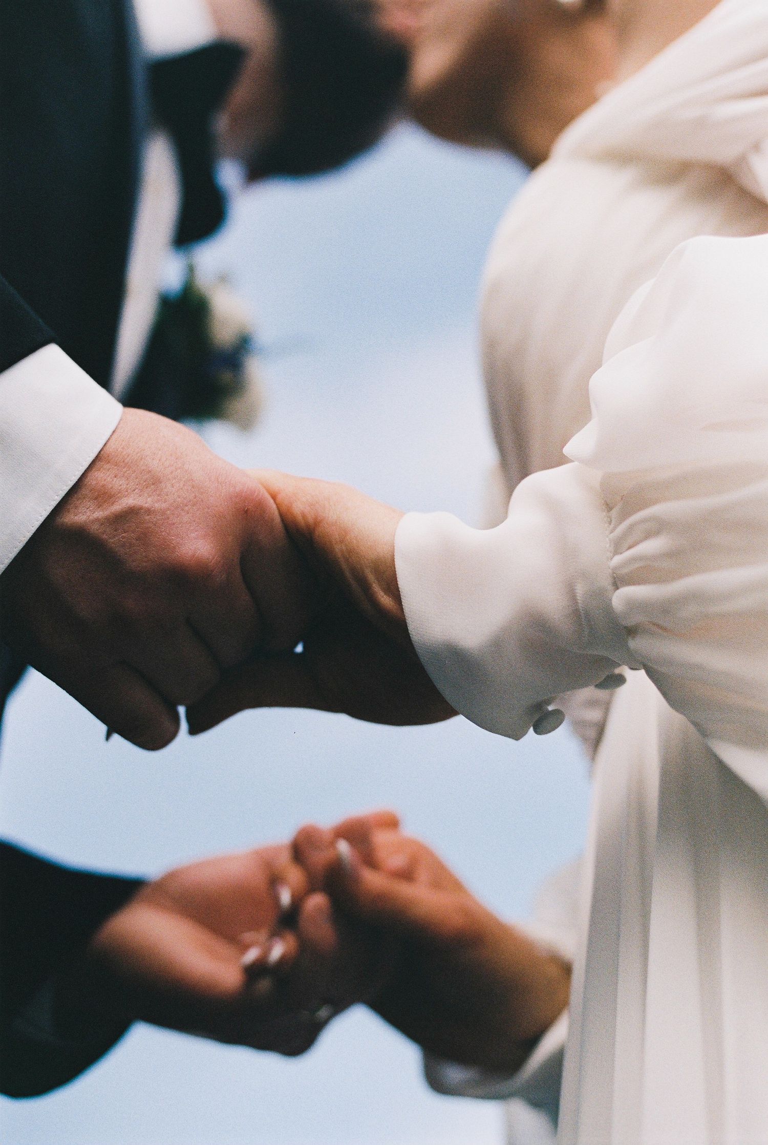 Close up of hands during a wedding ceremony showing delicate lace sleeves and tender gestures.