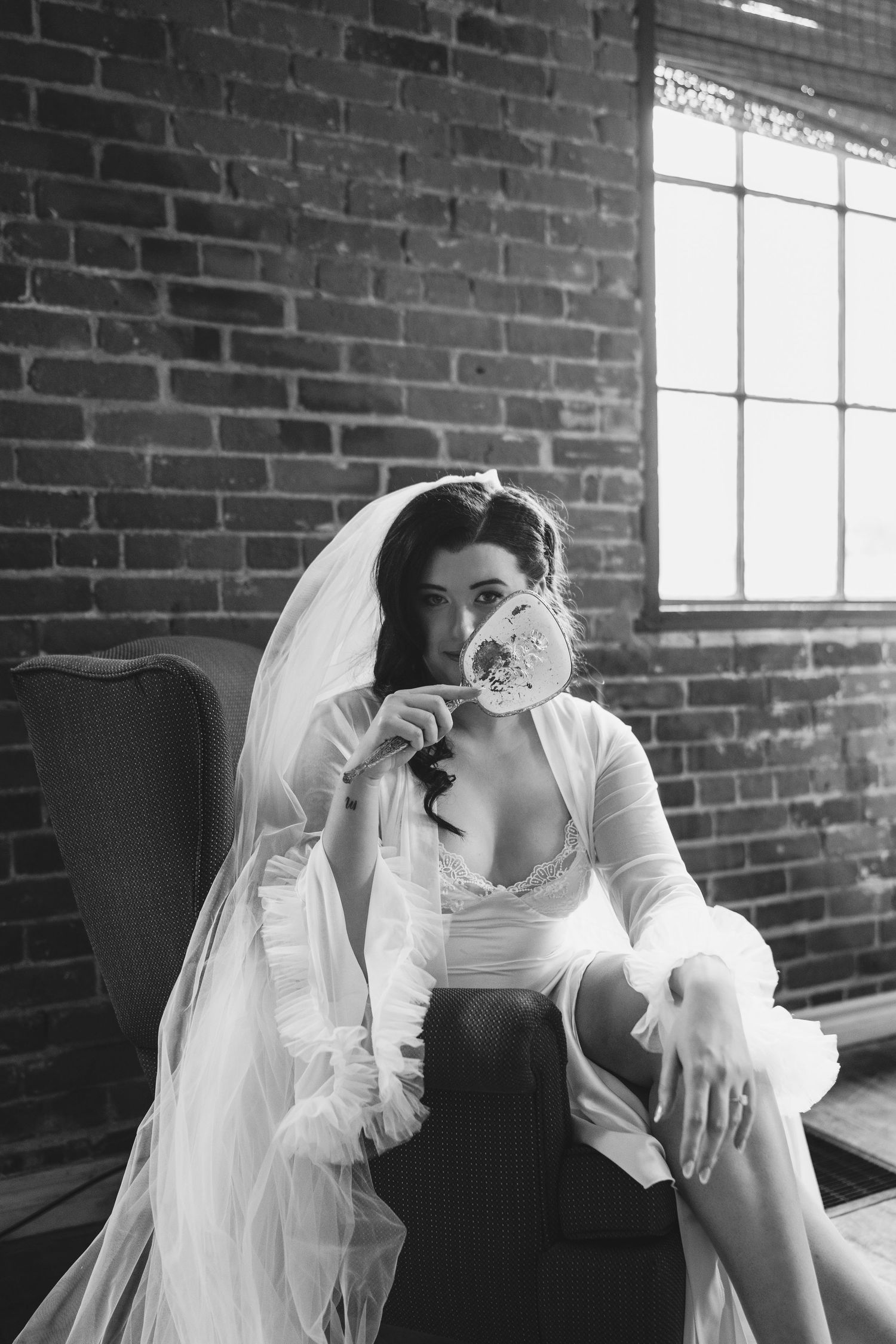 A bride in vintage-inspired attire sips from a teacup in a brick-walled room.
