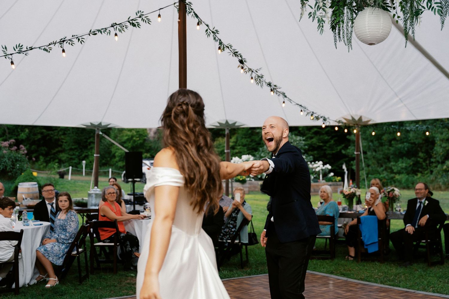 Wedding reception under a tent with string lights and floral decorations creating a romantic atmosphere.