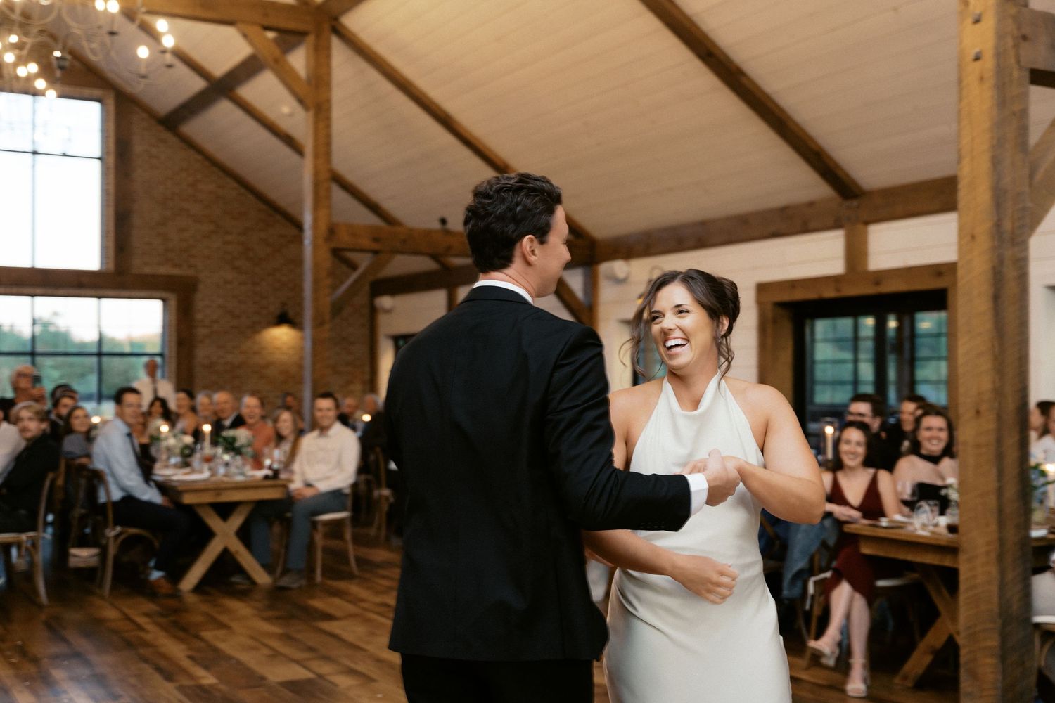 Wedding reception celebration inside a rustic wooden barn venue with exposed beams and white ceiling.