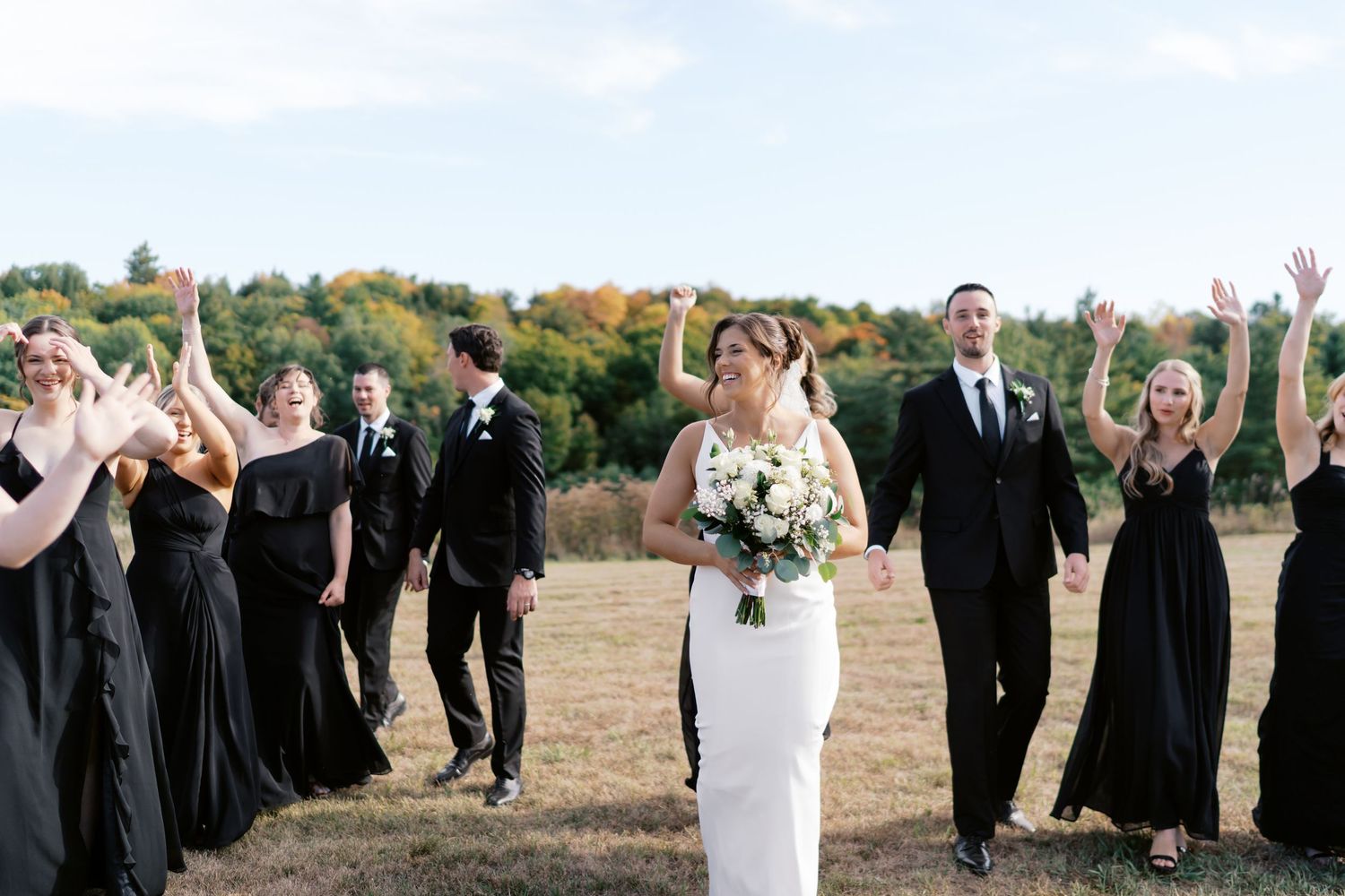 Wedding party in black dresses and suits poses together in an autumn field.