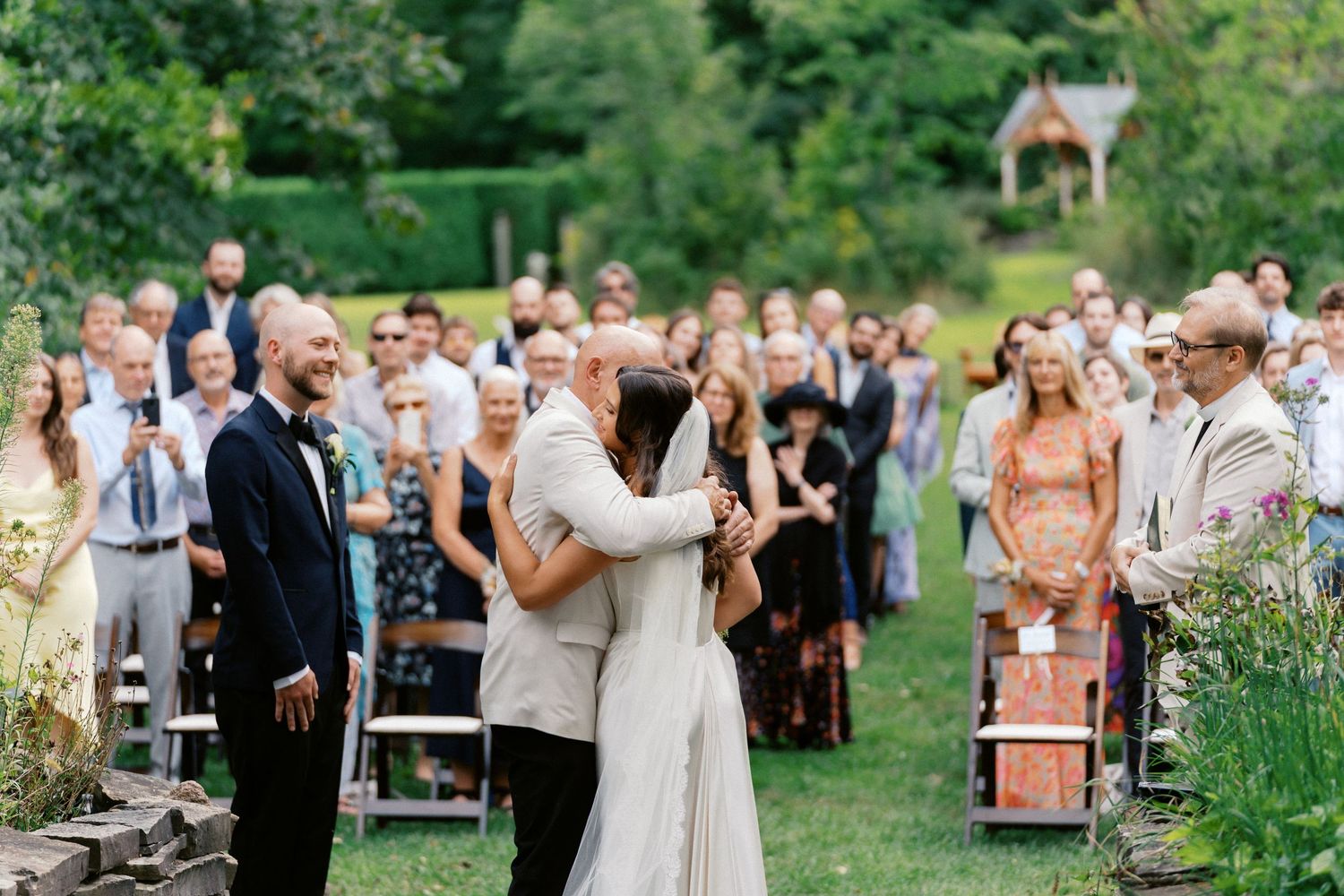 Wedding guests gather outdoors on a lush green lawn during a summer celebration.