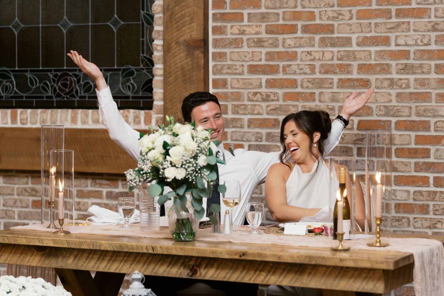 Wedding reception table setup with exposed brick wall and floral arrangements.