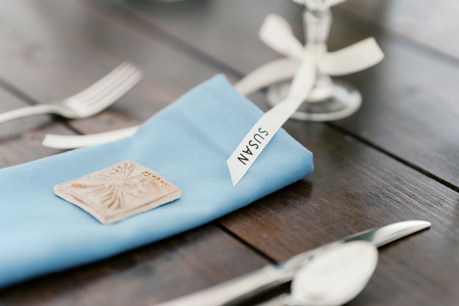 Light blue napkin with decorative place setting details on dark wooden table.