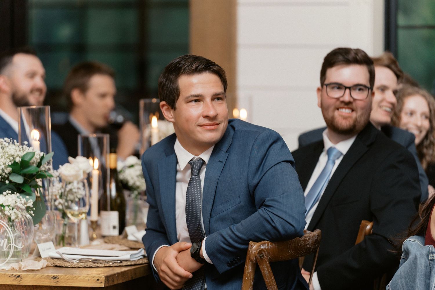 Wedding guests in formal attire seated at reception tables during dinner service.