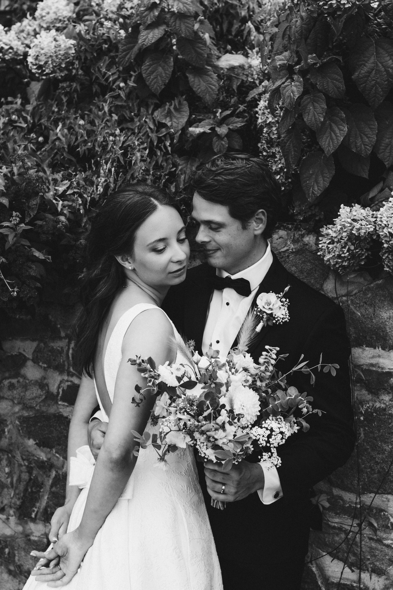 Black and white romantic portrait of newlyweds embracing among flowering vines.