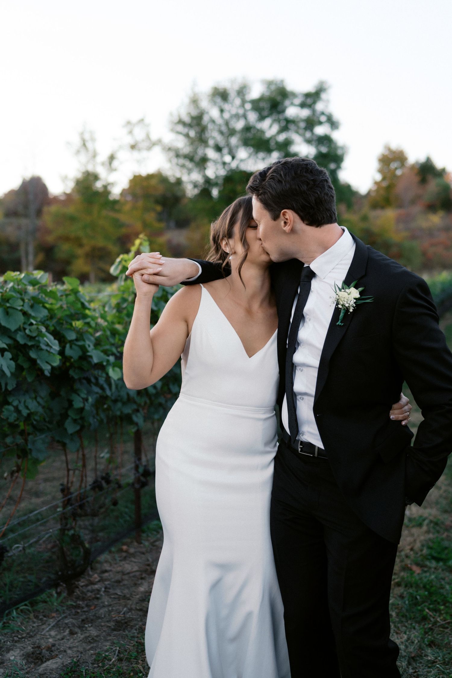 Romantic couple poses in a vineyard during sunset wearing classic black and white wedding attire.