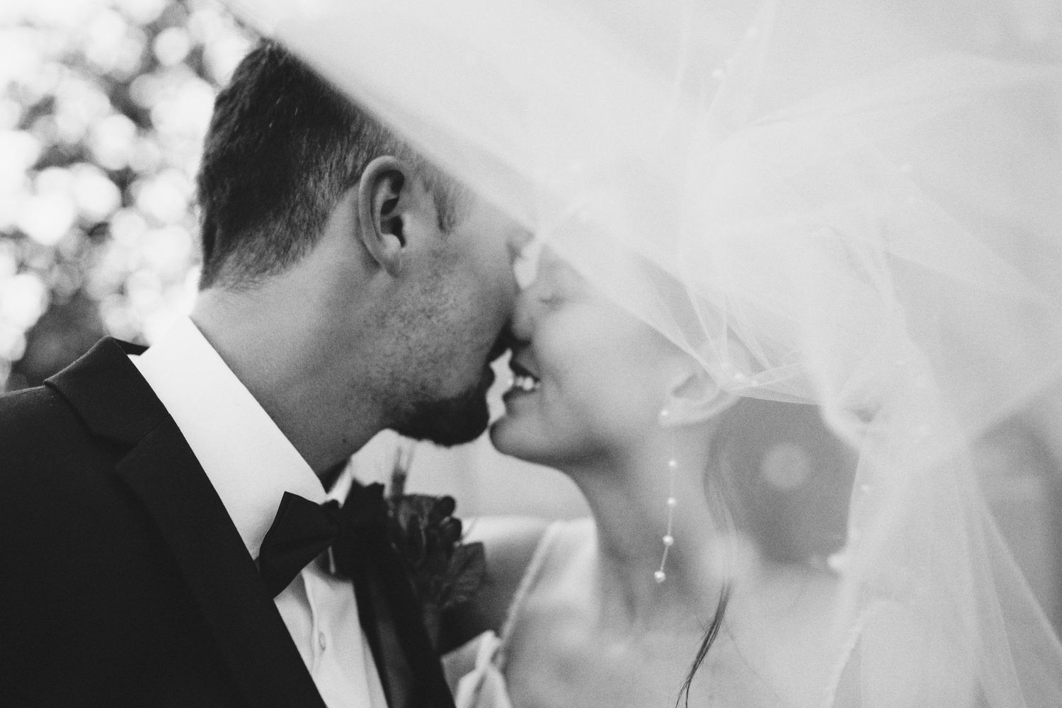 An intimate black and white wedding moment with a couple sharing a kiss under a flowing veil.