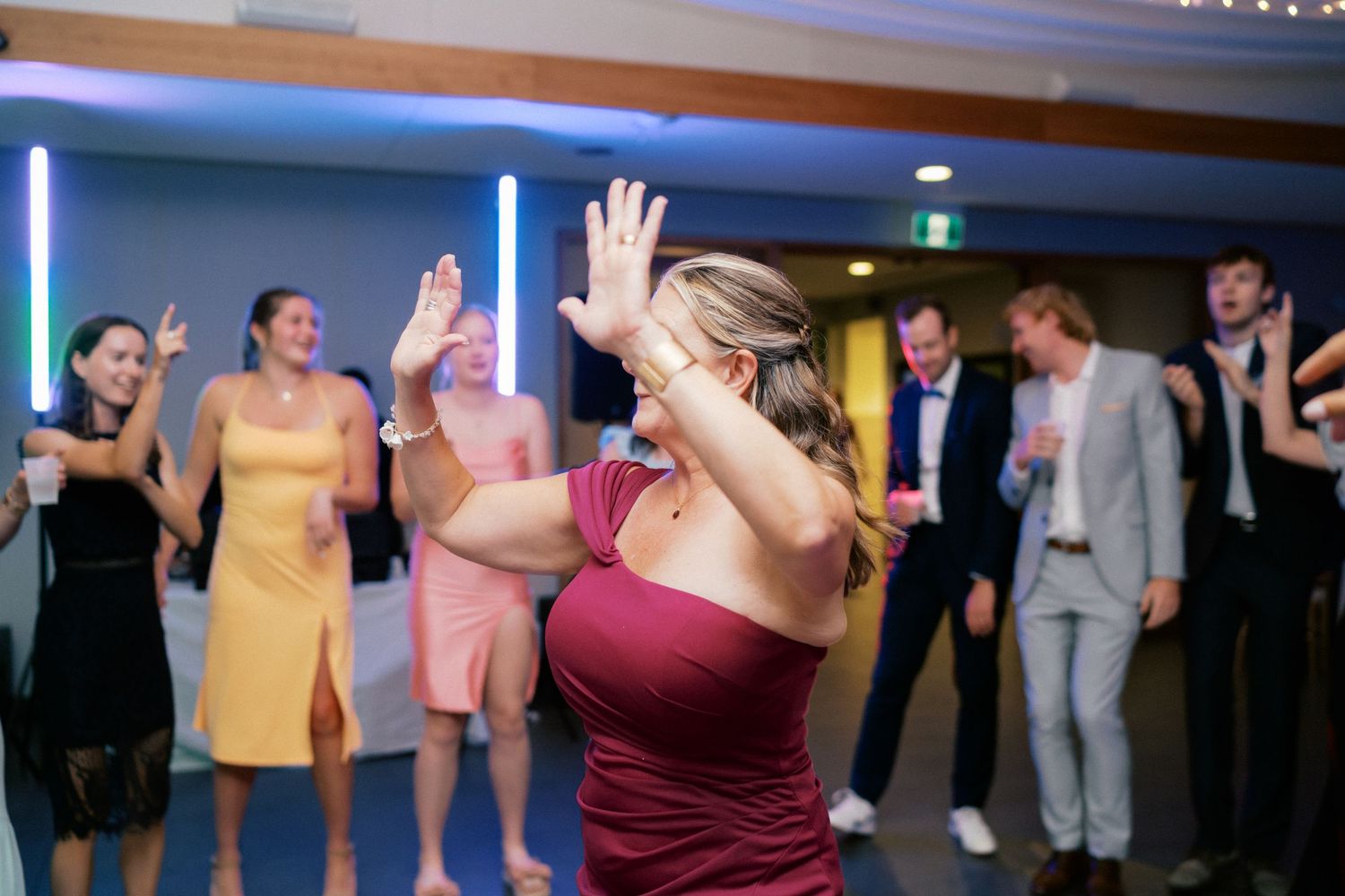 Wedding guests dancing energetically on the dance floor with colorful lights during a lively reception celebration.