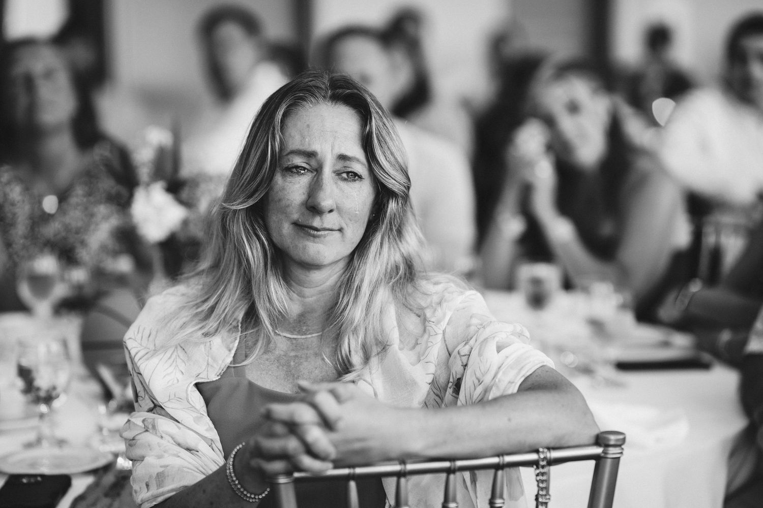 Black and white photo of a thoughtful woman with long hair sitting at a decorated event table.