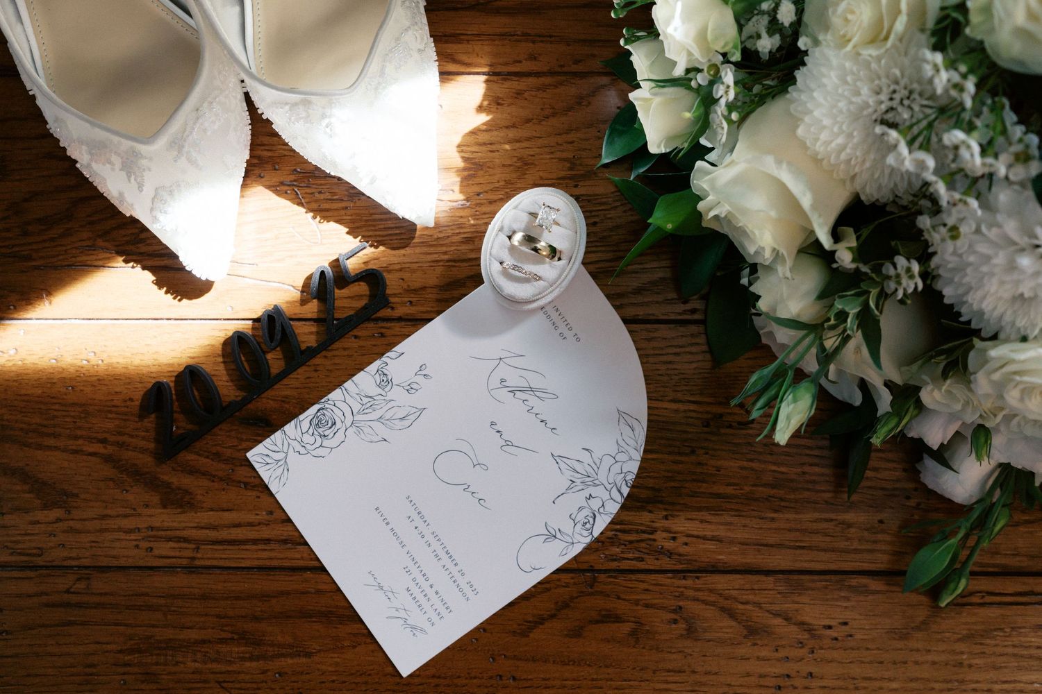 Wedding stationery and white floral arrangements displayed on rustic wooden surface.