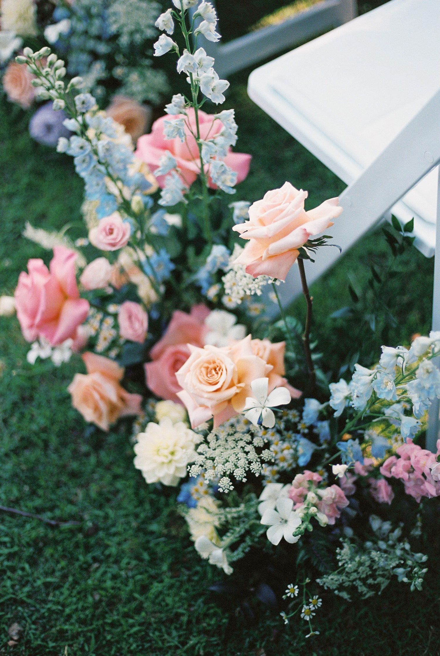 Delicate floral arrangements with pink roses and white flowers decorate an outdoor wedding setting.