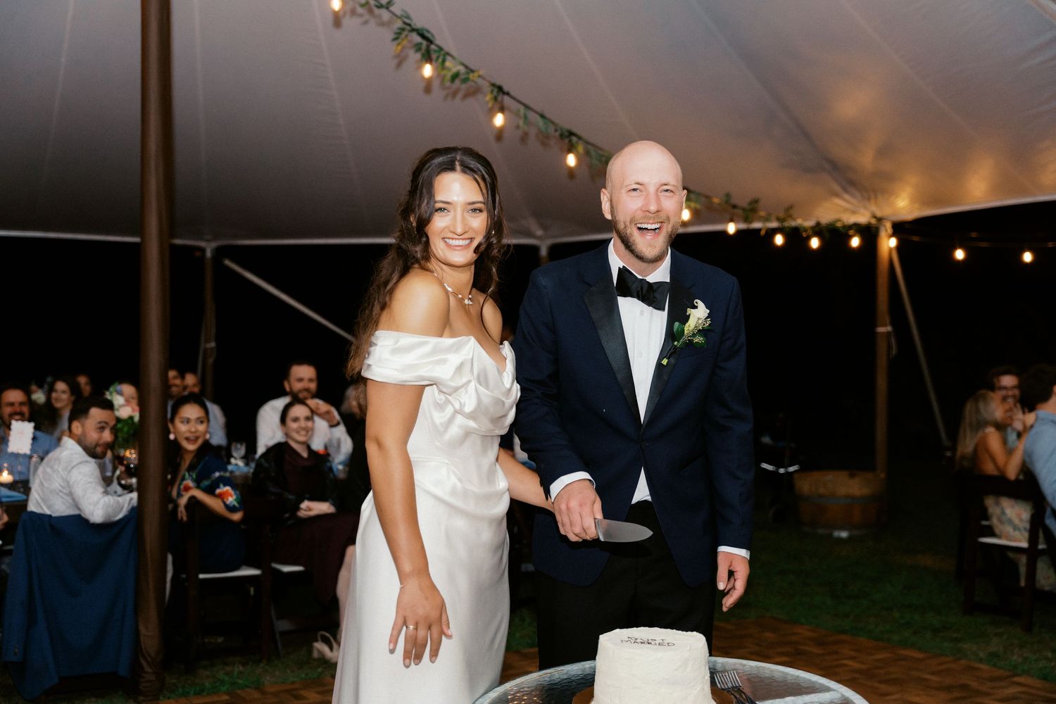 Wedding reception celebration under a tent with string lights and dancing guests.