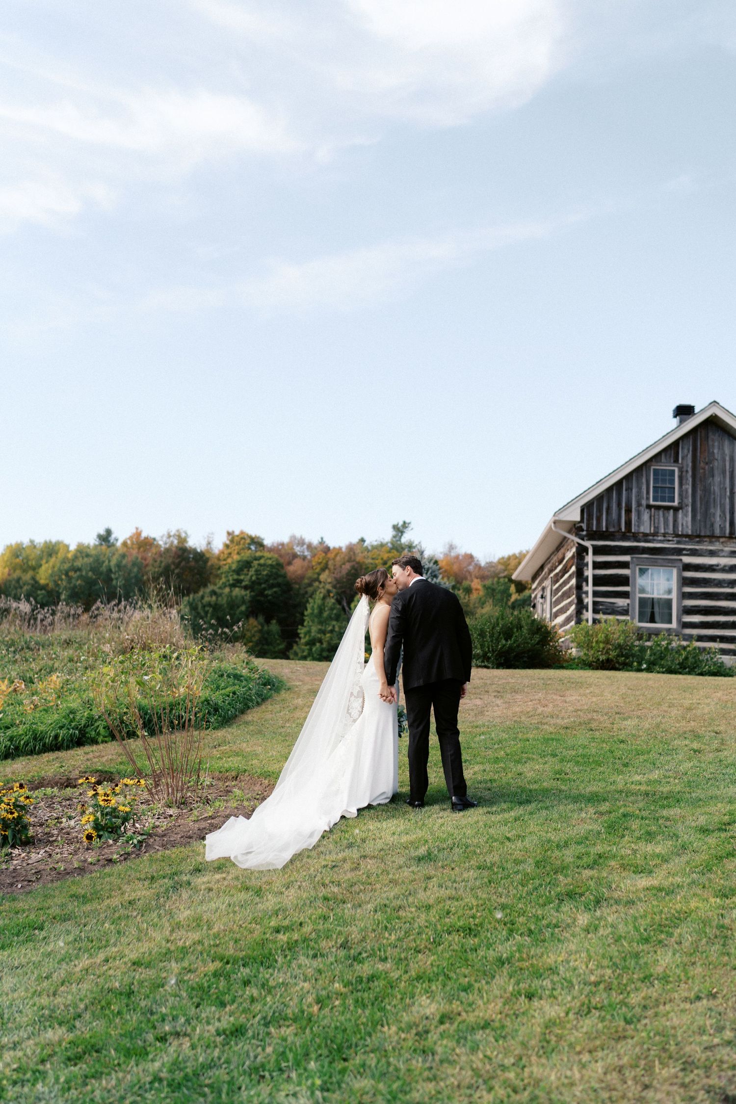 Wedding couple walking on a grassy hill with rustic barn buildings in the background.
