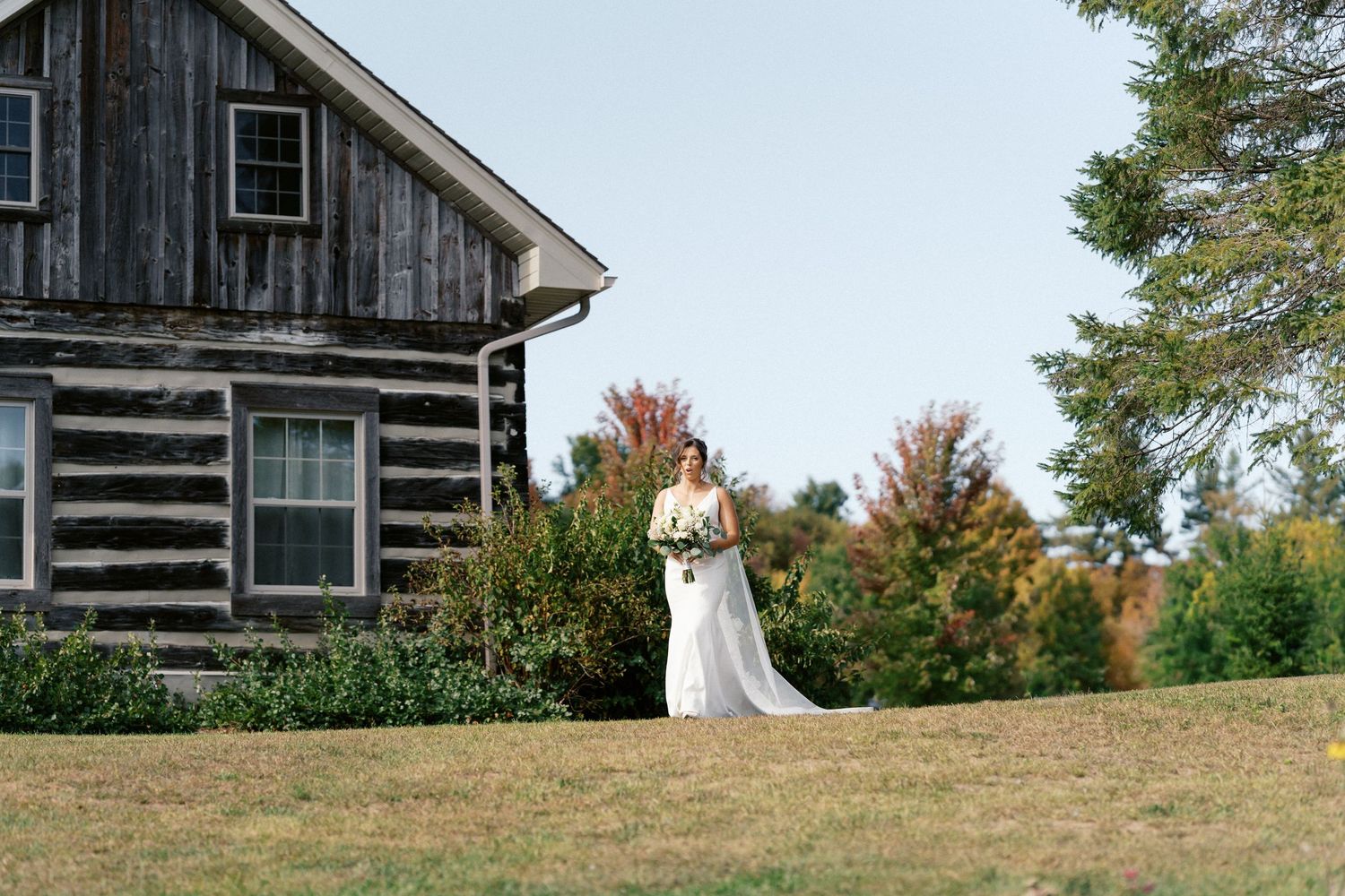 A wedding dress silhouette against a rustic log cabin surrounded by fall foliage.