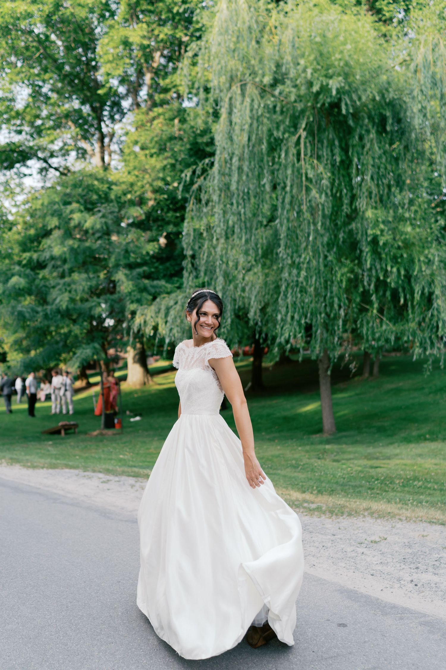 A white wedding dress flows elegantly as someone poses near a weeping willow tree in a park setting.