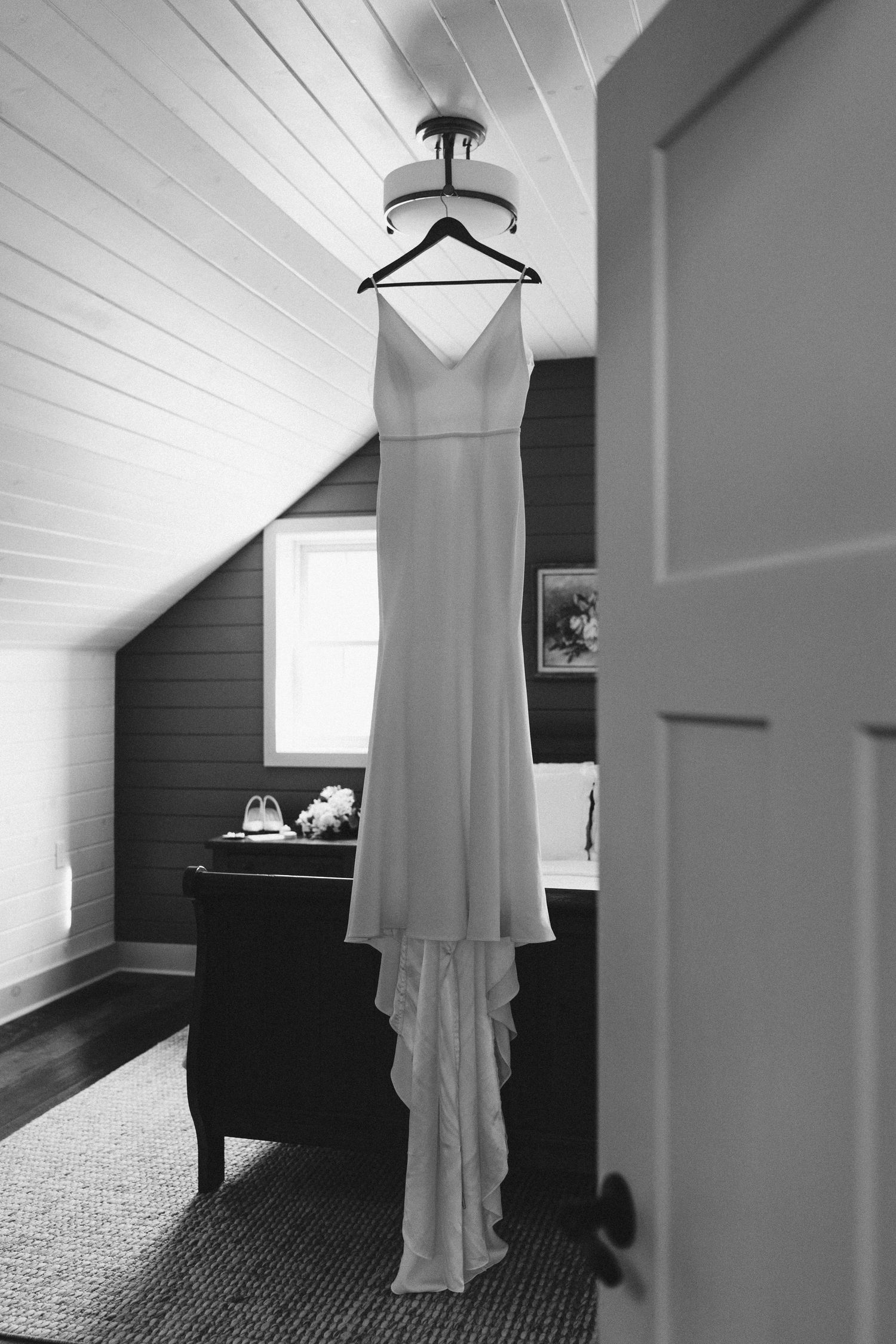 White wedding dress hanging in a room with sloped ceiling and natural light.