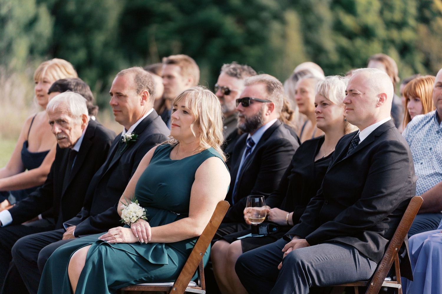 Wedding guests seated outdoors at a ceremony with a natural backdrop.