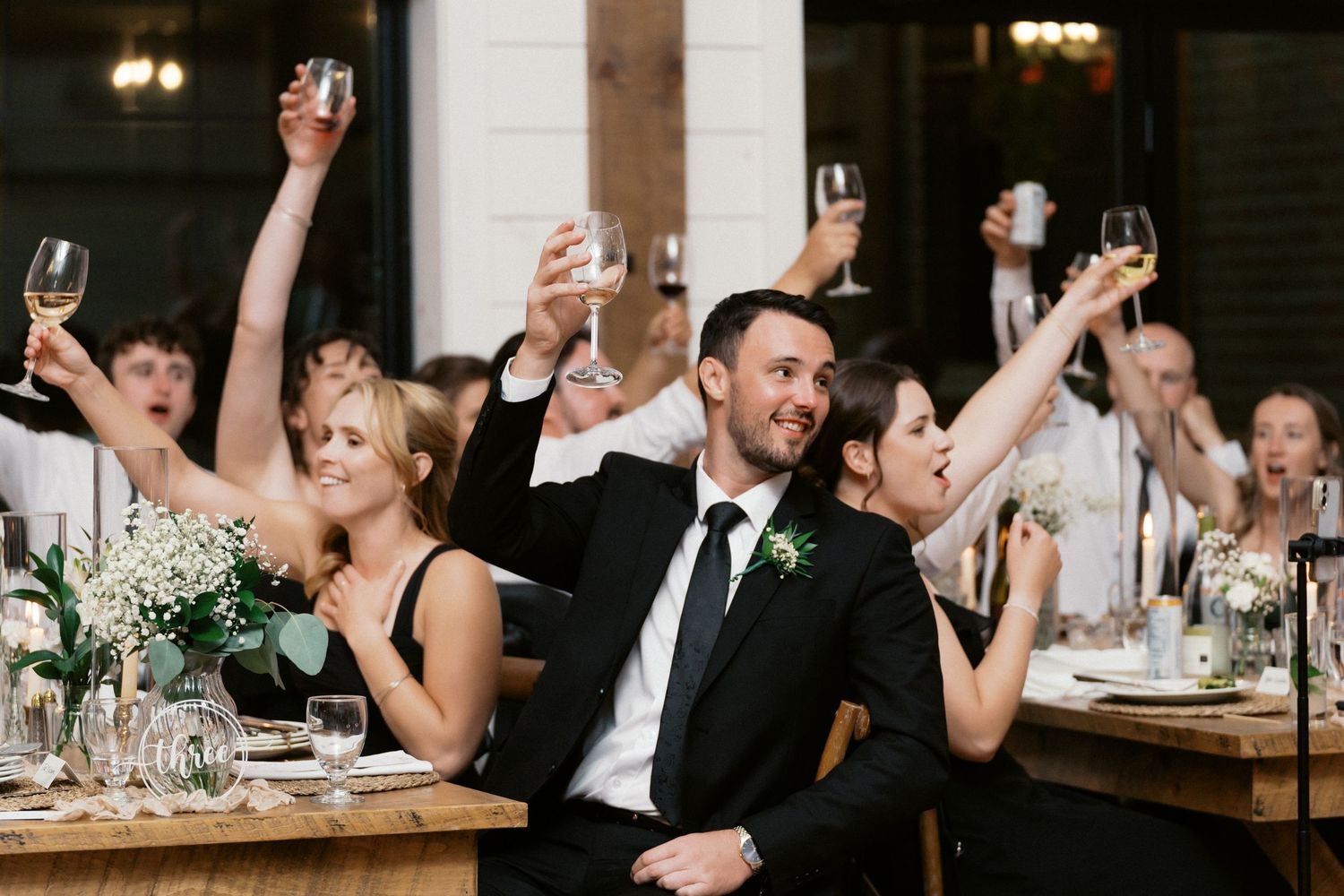 Wedding reception guests raising glasses in celebration at an indoor venue.