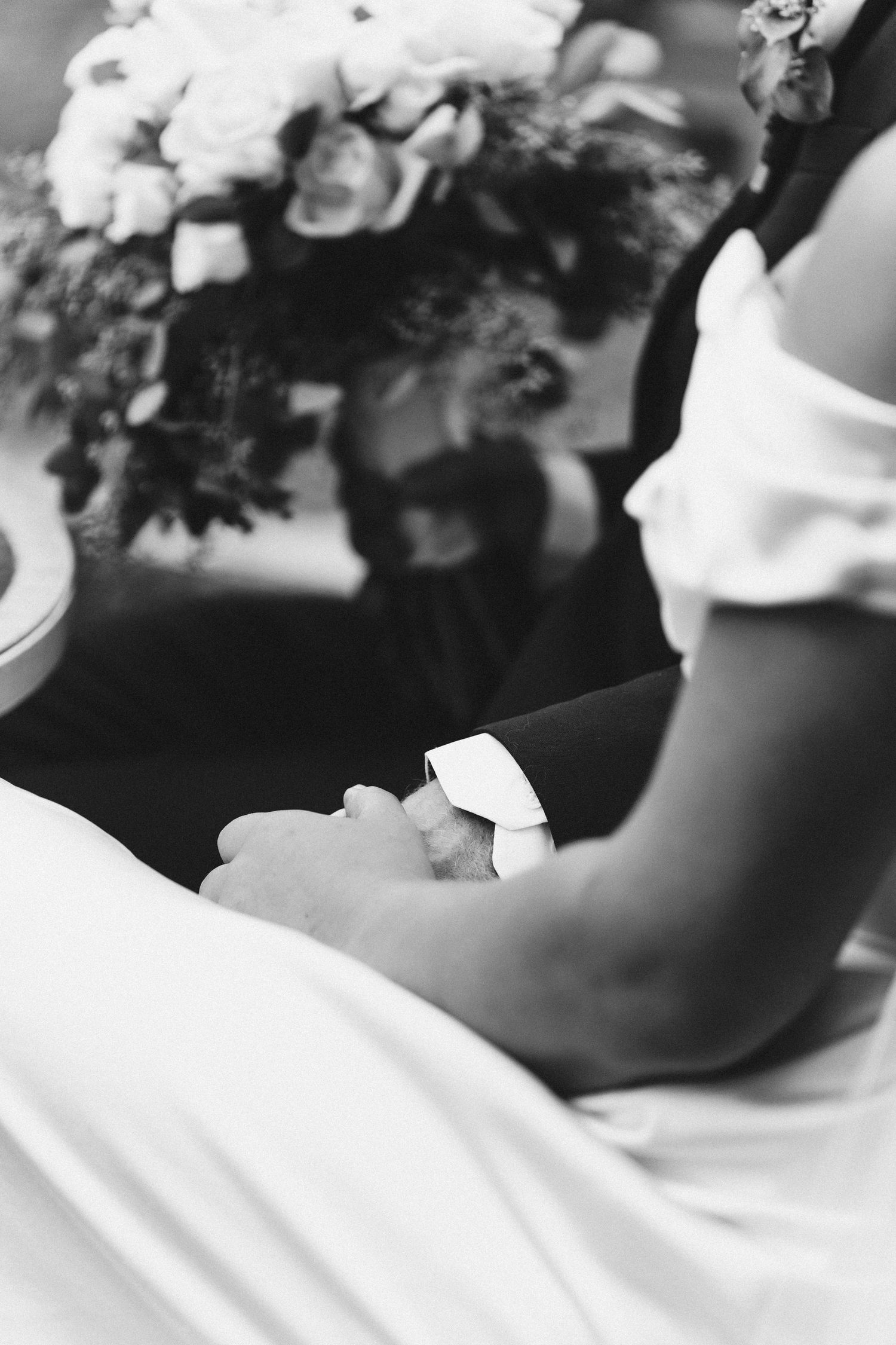 Artistic black and white close-up of a wedding dress detail with flowers in soft focus.