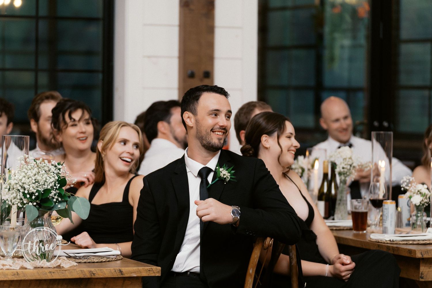 Wedding reception gathering with guests seated at tables in dimly lit venue.