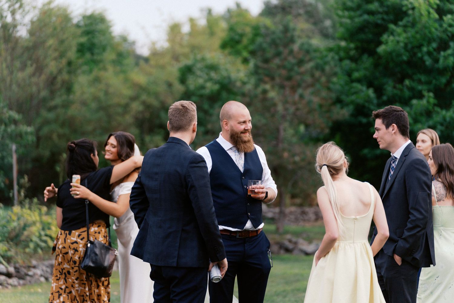 Wedding party mingles during outdoor cocktail hour in garden setting.