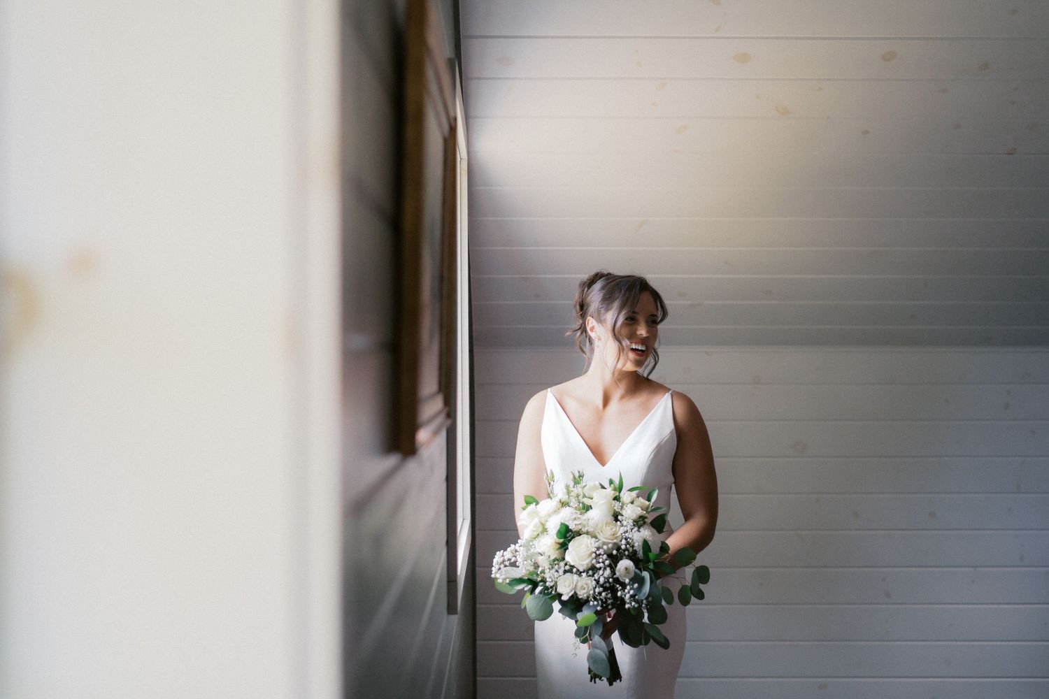 Soft, romantic bridal portrait with white bouquet against light background.