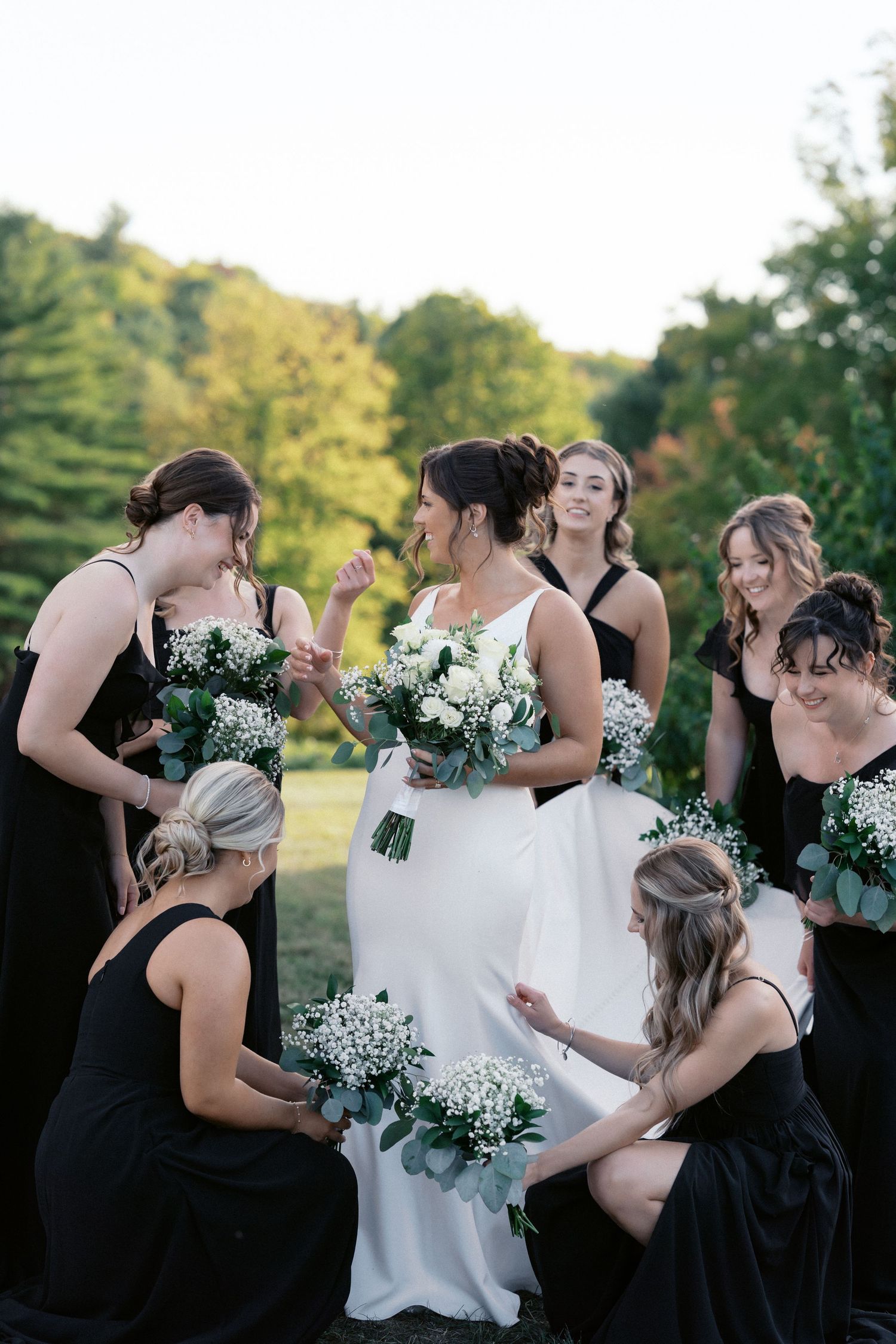 Bridesmaids in black dresses share joyful moments with the bride holding white floral bouquets.