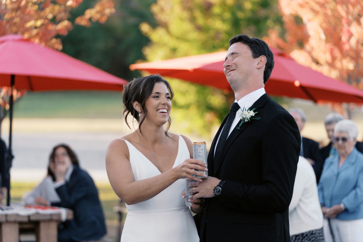 Wedding couple shares a dance under red umbrellas during their outdoor reception.