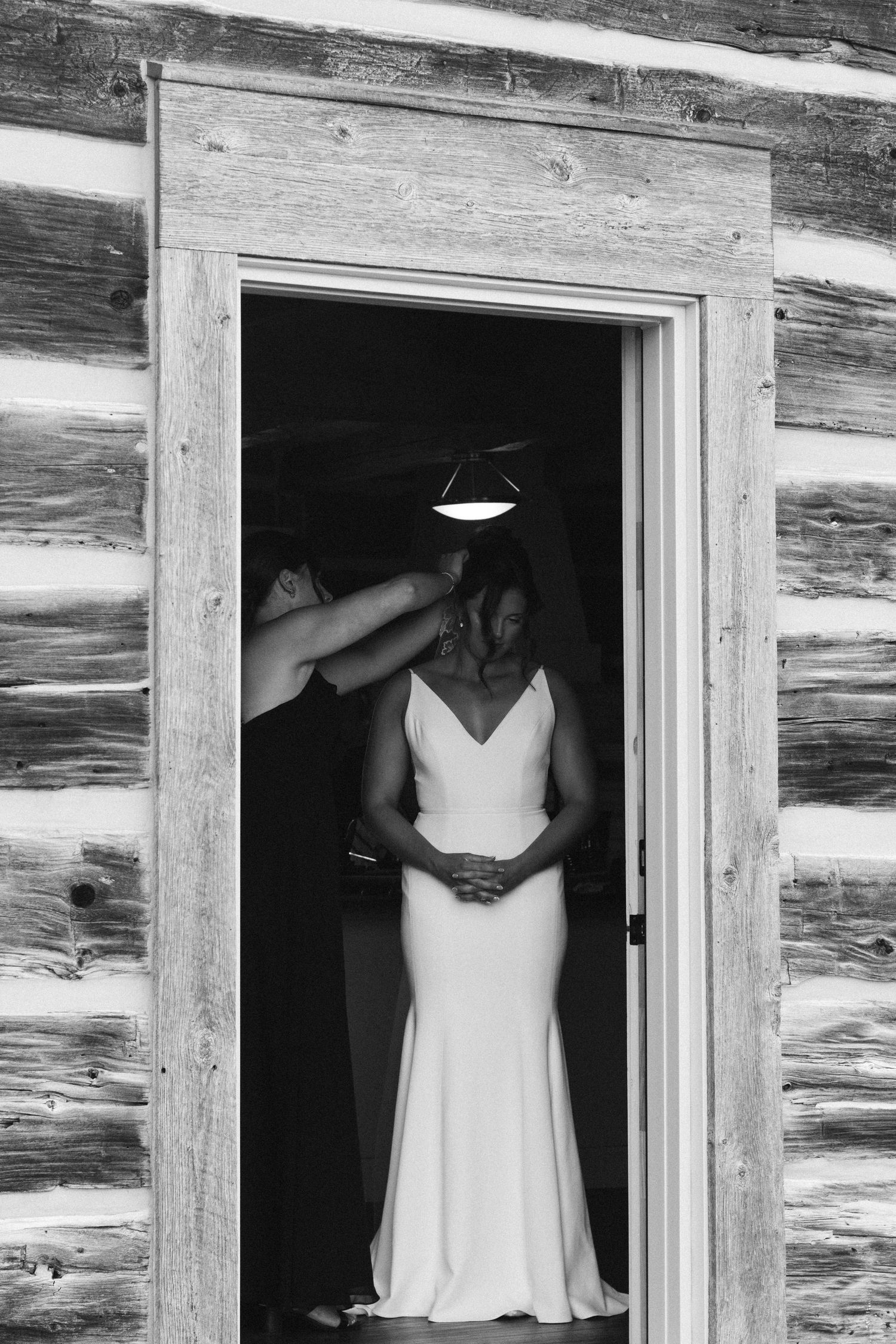 A white wedding dress hangs in the doorway of a rustic log cabin.