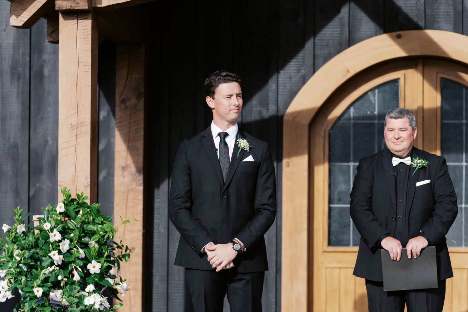 Wedding ceremony setup with wooden arch and formal attire at outdoor venue.