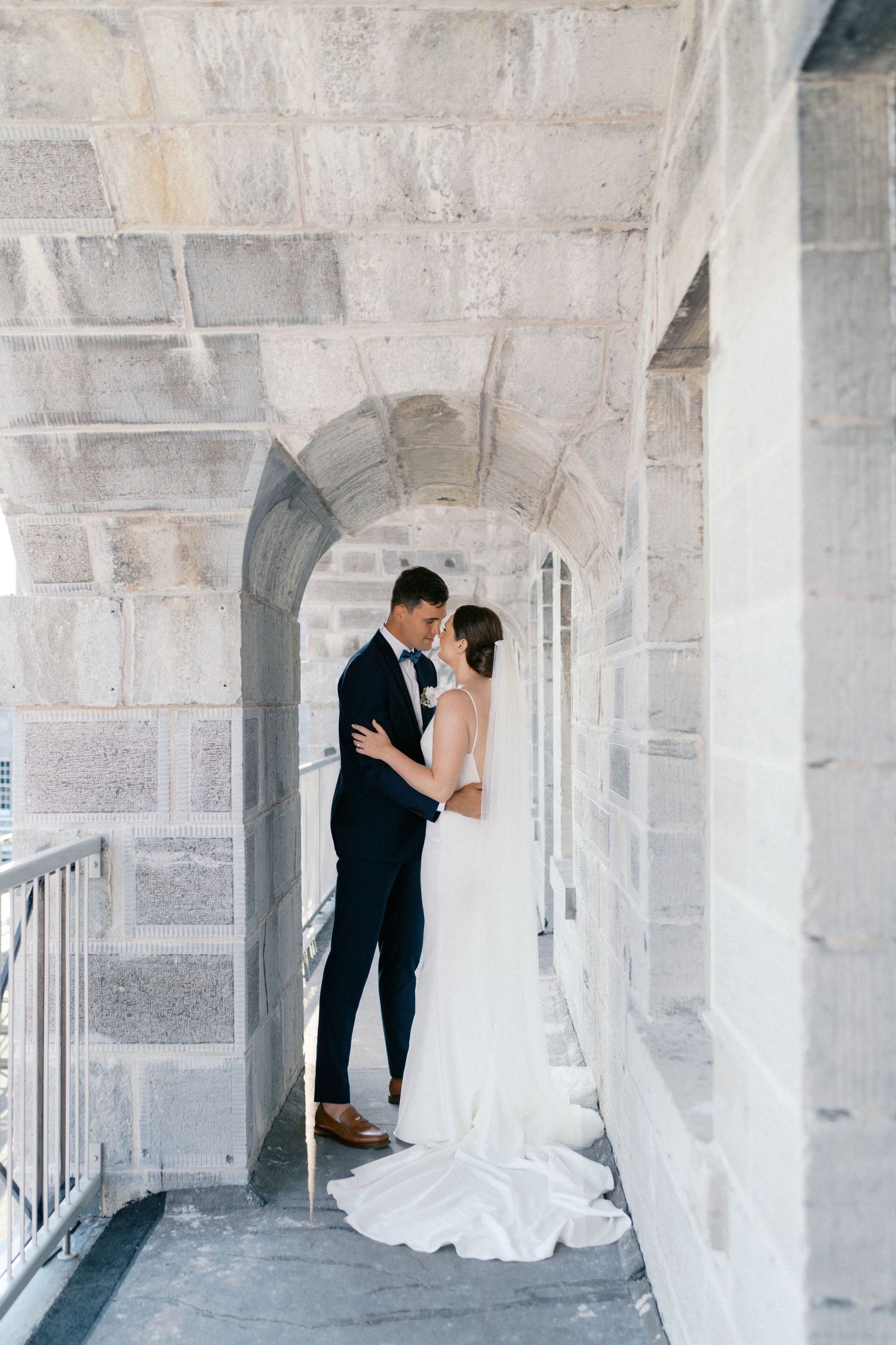 Bride and groom share a romantic embrace in a stone archway corridor on their wedding day.