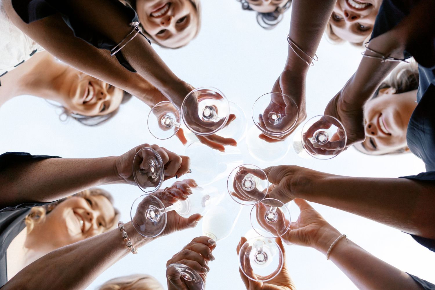 A group of people huddle together in a circle formation viewed from below against a bright white background.